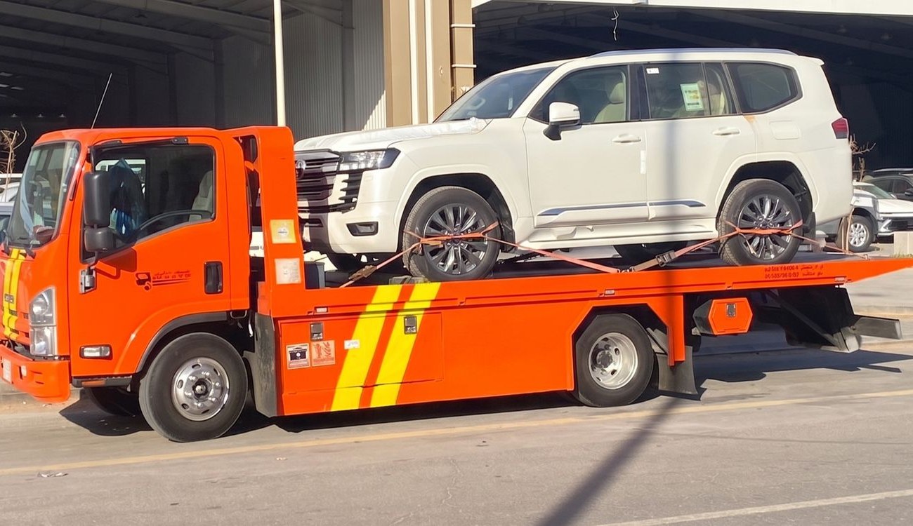 A Nashmi flatbed in Jeddah carrying a white Toyota Land Cruiser, secured with orange soft straps.